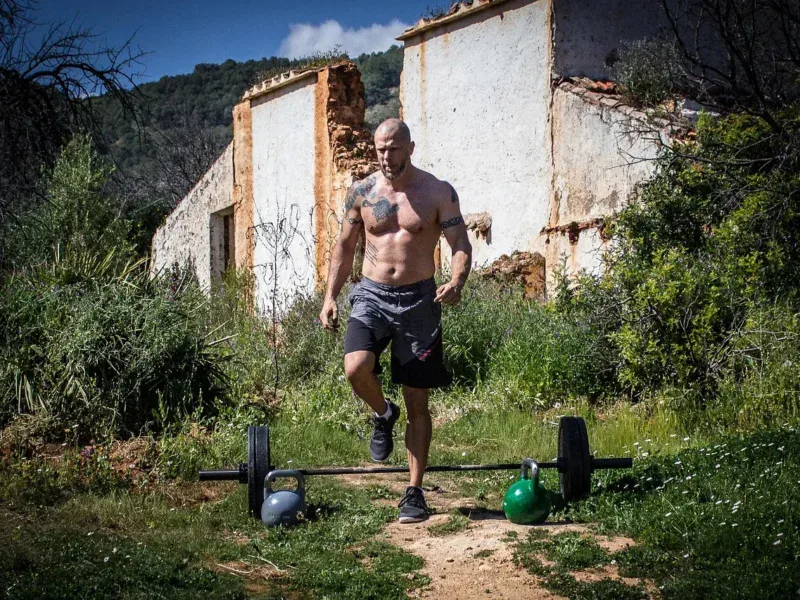 Mężczyzna biegnący w kierunku sztangi i odważników kettlebell na trawie