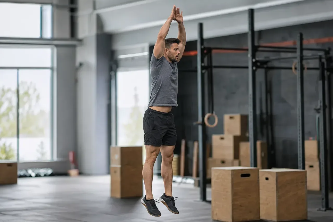 Mężczyzna w wyskoku z klaśnięciem nad głową kończy powtórzenie burpee w boksie crossfitowym