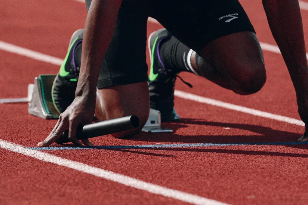Biegacz w blokach startowych na bieżni lekkoatletycznej z pałeczką sztafetową