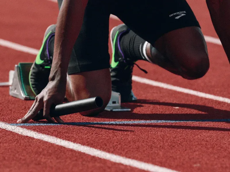 Biegacz w blokach startowych na bieżni lekkoatletycznej z pałeczką sztafetową